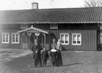 Claes och Ida Johansson med barnen Harald, Bertil, Ottilia och Karin på Idas arm. Klockaregården, Horred i bakgrunden. Foto från omkring 1915.